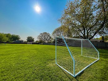 A soccer goal stands on a lush green field under a clear blue sky.